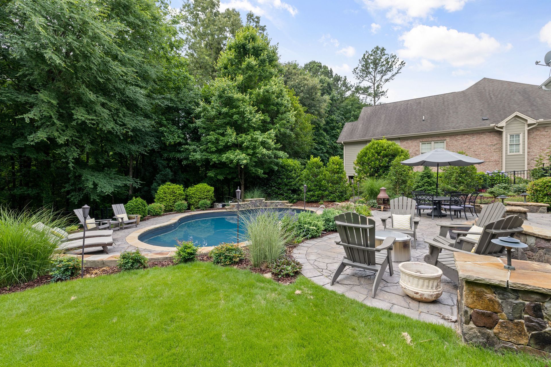 Charming backyard featuring a pool, patio with furniture, and lush greenery.