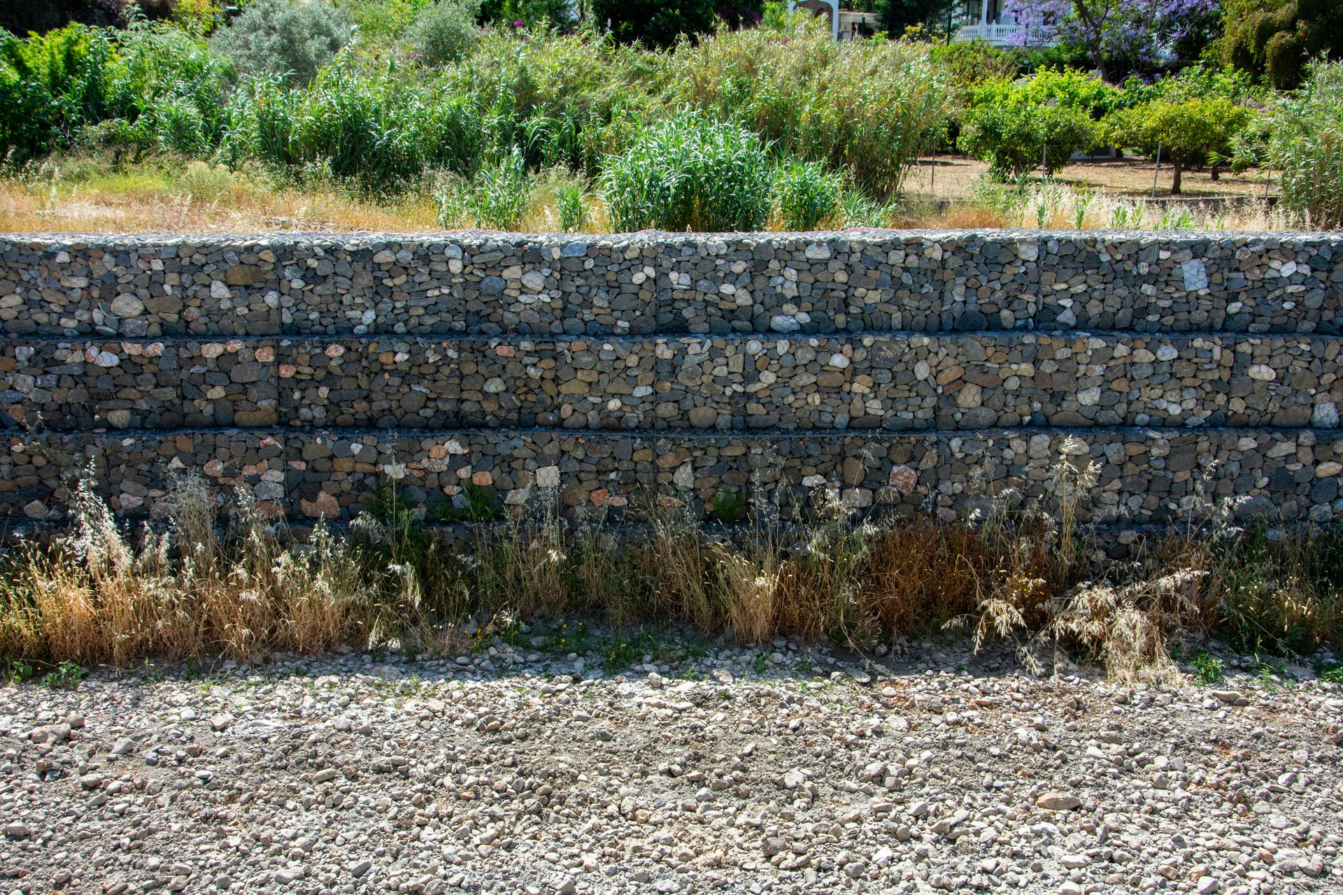 Stone gabion wall with dry grass and green plants